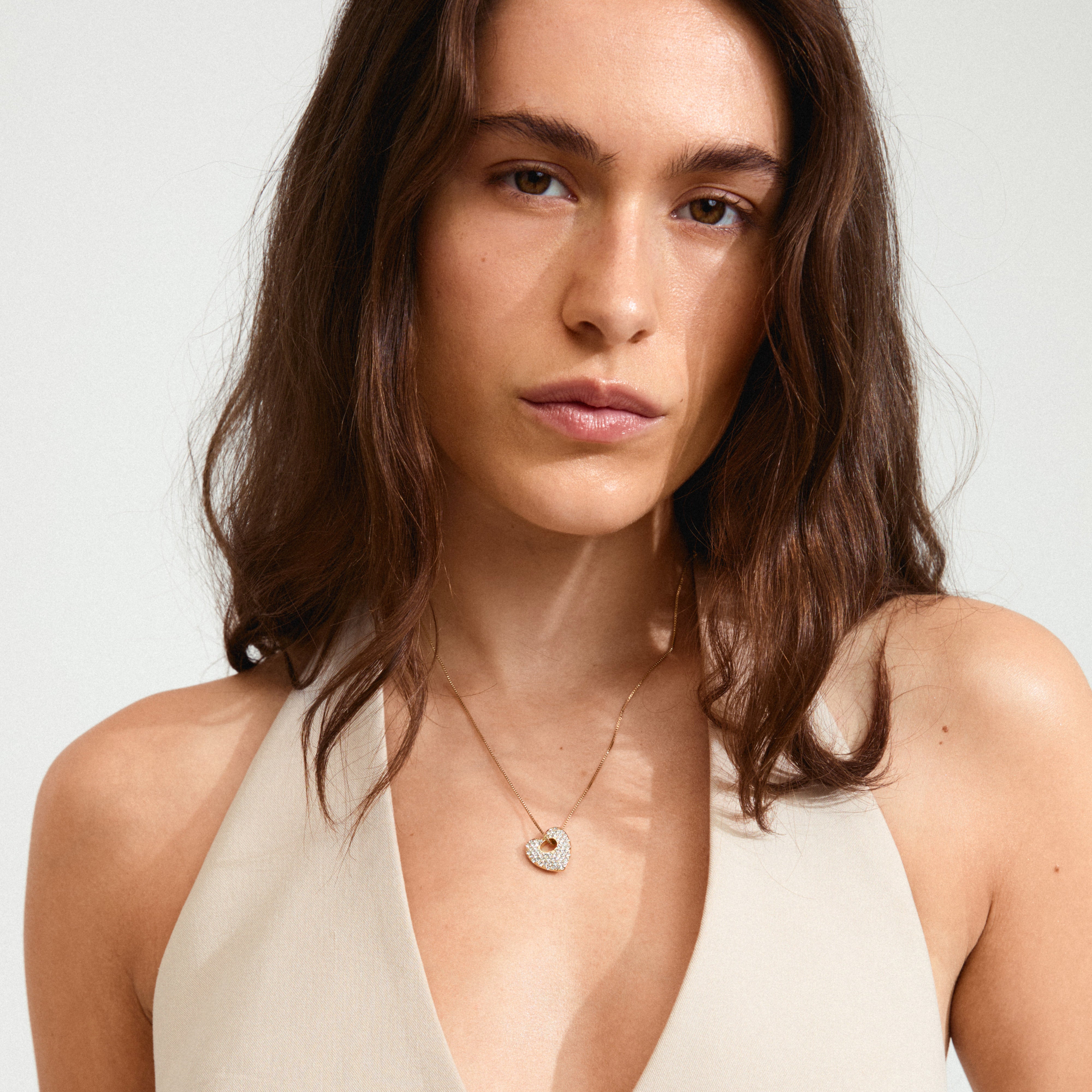 DUNE heart necklace gold-plated with sparkling crystals on a woman in a white dress, showcasing Pilgrim's elegant style and craftsmanship.