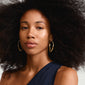 Close-up of a woman wearing Pilgrim's gold-plated DUNE hoop earrings, showcasing their large, sleek oval design and shiny finish.