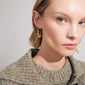 Close-up of a woman wearing Pilgrim's FOCUS gold-plated hoop earrings, featuring asymmetrical design with freshwater pearls, reflecting a luxury boho style.