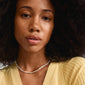 Woman wearing Pilgrim's TIDE necklace, featuring silver-plated beads, freshwater pearls, and glass beads, enhancing her yellow sweater, embodying Scandinavian style.