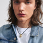 Man wearing a denim jacket showcasing the INTENT necklace by Pilgrim, featuring a black leather cord with a teardrop-shaped, gold-plated pendant.