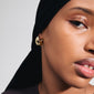 Woman wearing INTENT earrings gold-plated; chunky, shiny semi-hoops from Pilgrim, complementing her black head scarf and shirt, embodying modern elegance.