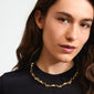 SUNSET necklace gold-plated, featuring a bold, wavy design, worn by a woman with long brown hair, black shirt, and gold necklace.