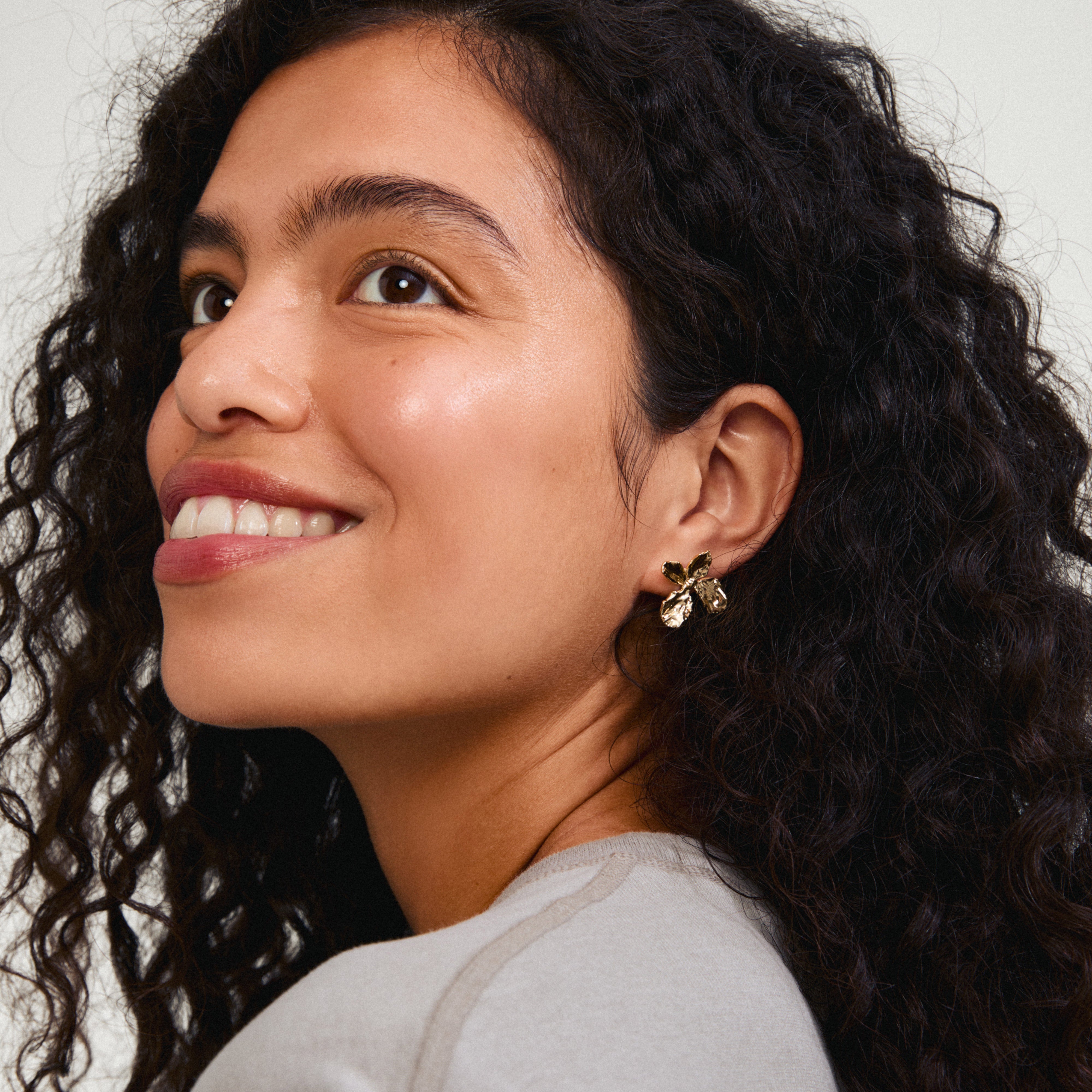 Gold-plated DREAM earrings with a floral design, worn by a smiling woman with curly hair, showcasing Pilgrim's handcrafted elegance and Scandinavian inspiration.