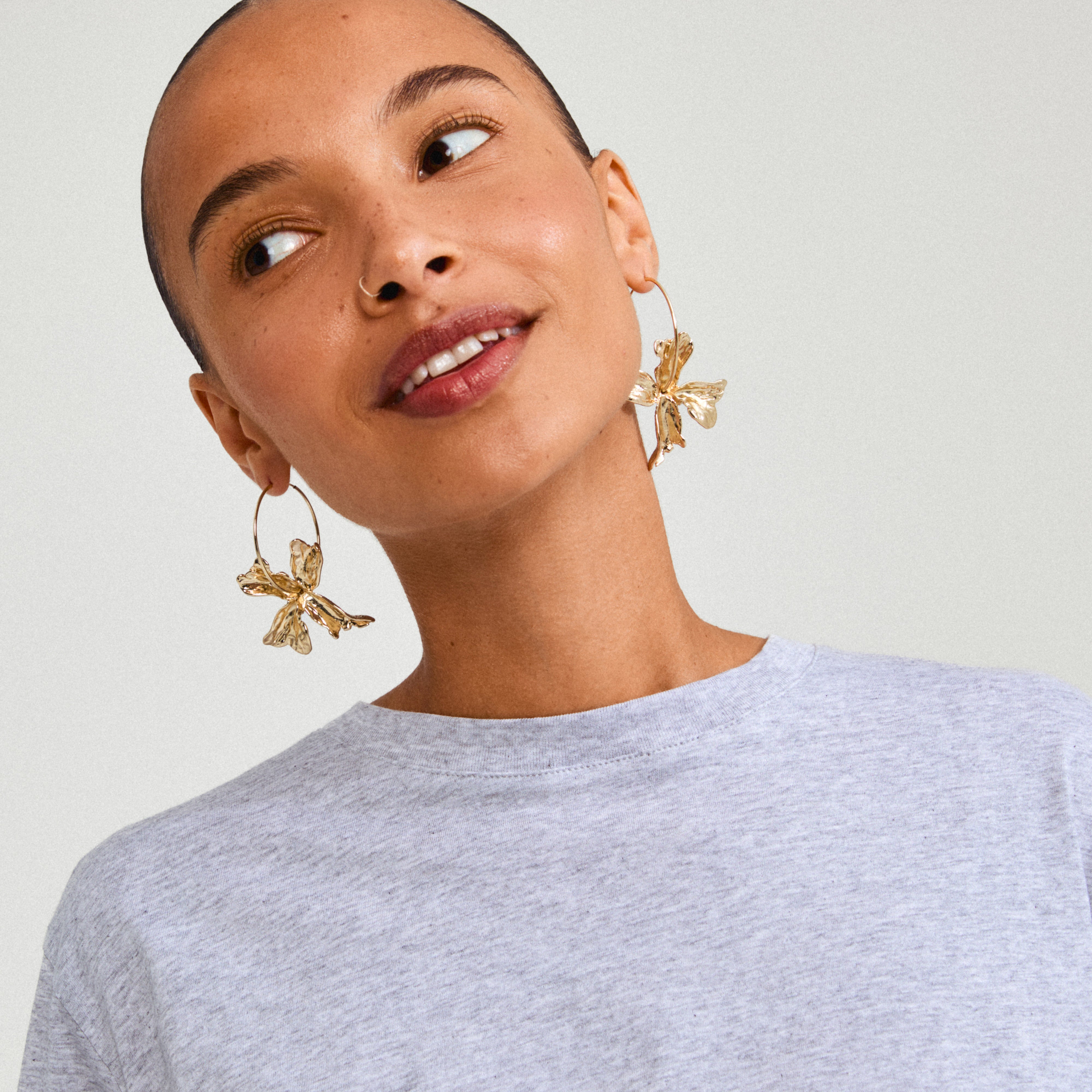 Woman wearing Pilgrim's DREAM hoops gold-plated earrings, featuring slender hoops and a flower pendant, embodying a luxurious boho vibe.