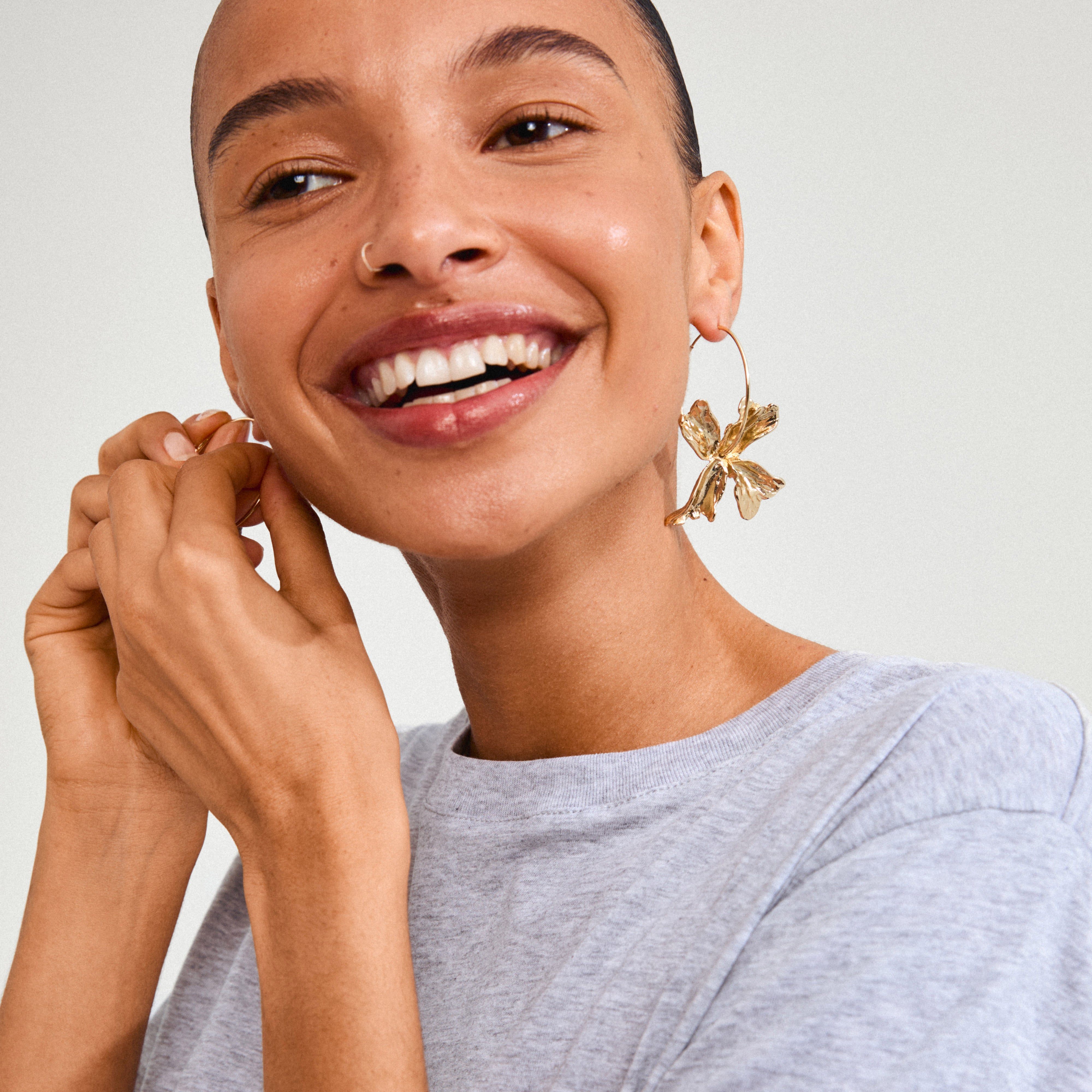 Woman smiling, showcasing Pilgrim's DREAM hoops gold-plated earrings with a prominent flower pendant, embodying a luxurious boho vibe for a trendy summer look.