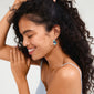 Woman with curly hair wearing Pilgrim's DREAM hoops, silver-plated with Green Aventurine and Topaz detailing, smiling elegantly.