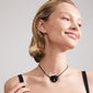 STAY black agate necklace with a large heart pendant on a black leather cord, worn by a smiling woman. Gold-plated chain adds a bohemian touch.