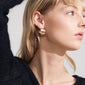 TALULLA earrings gold-plated, ultra-wide hoops with glossy shine, worn by a woman in a black sweater, showcasing trendy, recycled Danish jewelry from Pilgrim.