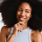 Woman smiling while holding a gold-plated RYAN ring with a heart design, showcasing Pilgrim's IMAGINATION collection's vibrant, handcrafted jewelry.