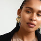 Woman with braids wearing heart-shaped, gold-plated RYAN earrings from Pilgrim, showcasing a rustic, handcrafted design perfect for a luxe boho look.