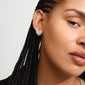 Close-up of Pilgrim's DUNE silver-plated heart-shaped earrings, adorned with Preciosa crystals, worn by a woman with braided hair.