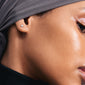 Close-up of a woman wearing the PELAGIA single earring, a silver-plated, organically-shaped micro stud from Pilgrim, showcasing its reflective rustic surface.