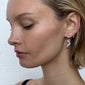 Woman showcasing a PELAGIA single silver-plated earring by Pilgrim, featuring a unique organic shape and rustic surface for a confident, elegant look.