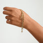 Gold-plated chain bracelet on a hand, featuring the CHARM symbols pendant with cross, anchor, and heart, representing personal style and deep values.