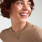 Woman smiling wearing the CHARM love pendant gold-plated necklace from Pilgrim, featuring a glossy pink enamel and crafted from recycled materials.