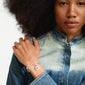 Woman with afro hair wearing a denim jacket shows Pilgrim's CHARM crystal heart pendant silver-plated, detailed with Preciosa crystals and a silver chain bracelet.