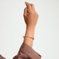 KIRA bracelet gold-plated: A close-up of a hand wearing Pilgrim's sleek, gold-plated bangle adorned with sparkling crystals, featuring a discreet click clasp.