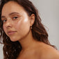 IBEN tree-of-life hoop earrings, gold-plated with coin pendants and discreet crystals, worn by a woman with long brown hair.