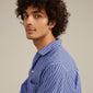 Man with curly hair wearing blue-striped shirt showcases EZO twirled crystal hoops gold-plated, featuring twisted details and Preciosa crystals for a chic look.