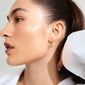 Close-up of a woman wearing Pilgrim's CHARMAINE gold-plated hoop earrings with flower pendants, showcasing their elegant, summery design.