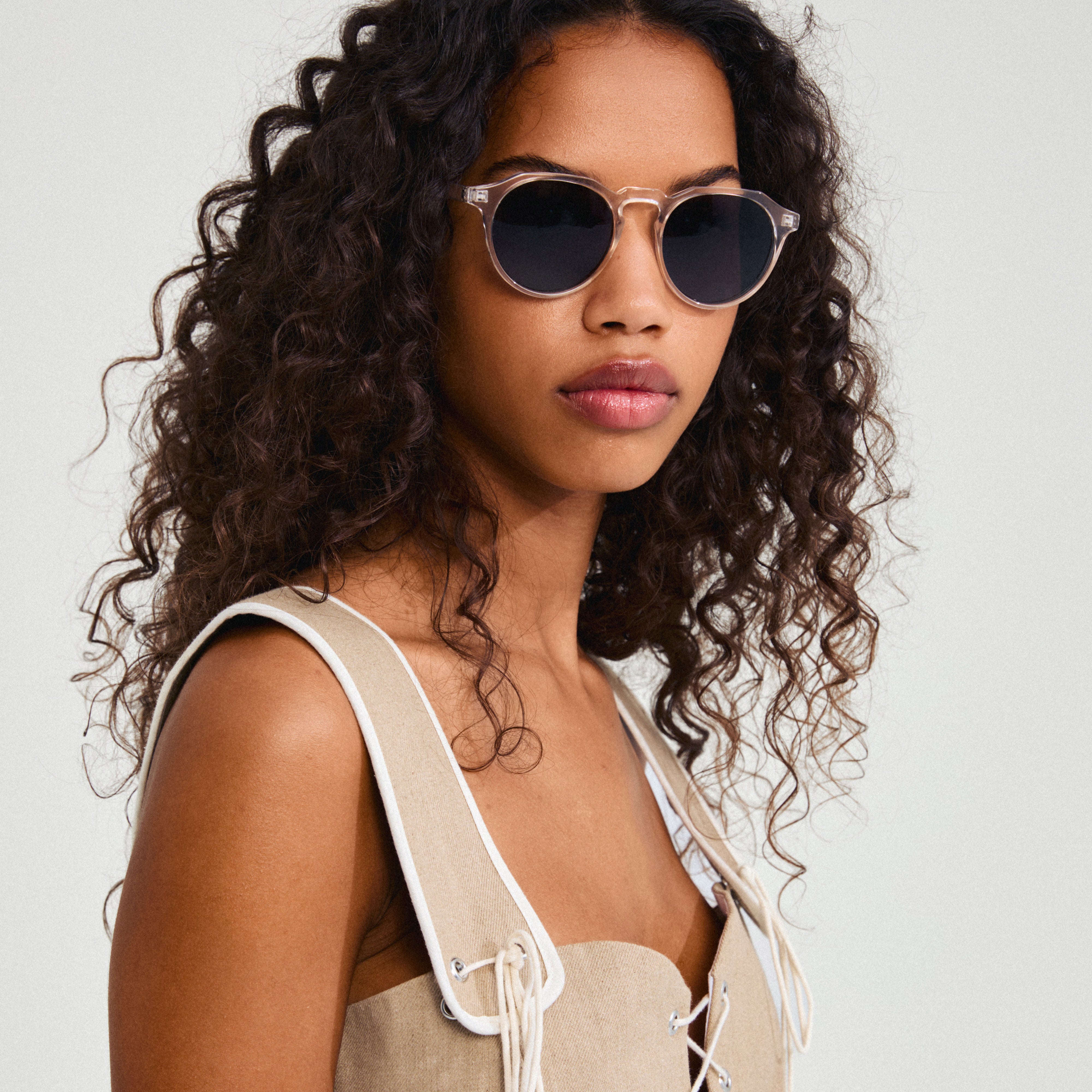 Woman wearing ALEJANDRA sunglasses with crystal clear frames and smoke-colored lenses, showcasing a chic and modern accessory from Pilgrim's collection.