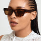 Woman wearing ASHLYN sunglasses, showcasing angular design with a confident, trendy vibe. Perfect for spring fashion, offering UV protection and eco-friendly materials.