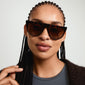 A woman models Pilgrim's ALESSANDRA sunglasses in tortoise brown, featuring a sleek, horizontal design with UV400 lenses and stylish empowerment.