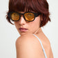 Woman with short red hair wearing ARIAH sunglasses featuring wide temples and yellow lenses, embodying a trendy, eco-friendly design from Pilgrim.