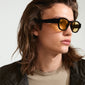 Man with long hair wearing the ARIAH sunglasses with wide temples and yellow lenses, embodying coolness and energy.