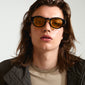 Man with long hair wearing ARIAH sunglasses featuring wide temples and yellow lenses, embodying luxury and coolness.