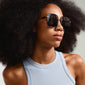 Woman modeling AYLIN sunglasses with oversized smoke lenses and gold temples, capturing a trendy 70s vibe for a stylish, modern summer look.