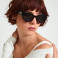 A woman with short red hair wearing AUBREE sunglasses, featuring a sleek black cat-eye frame adorned with sparkling crystals, ideal for a stylish summer look.