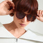 Woman with short red hair wearing Vanille sunglasses featuring slim gold-plated temples and a sleek dark brown frame from Pilgrim's summer collection.