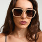 Woman wearing ADDILYN sunglasses with oversized square frames, featuring metal temples and cut-out detailing, embodying a retro, stylish vibe. Designed by Pilgrim with UV protection.