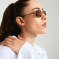 Woman wearing AMIYAH sunglasses by Pilgrim, featuring brown lenses and an edgy metal frame, holding her shoulder in a stylish pose.